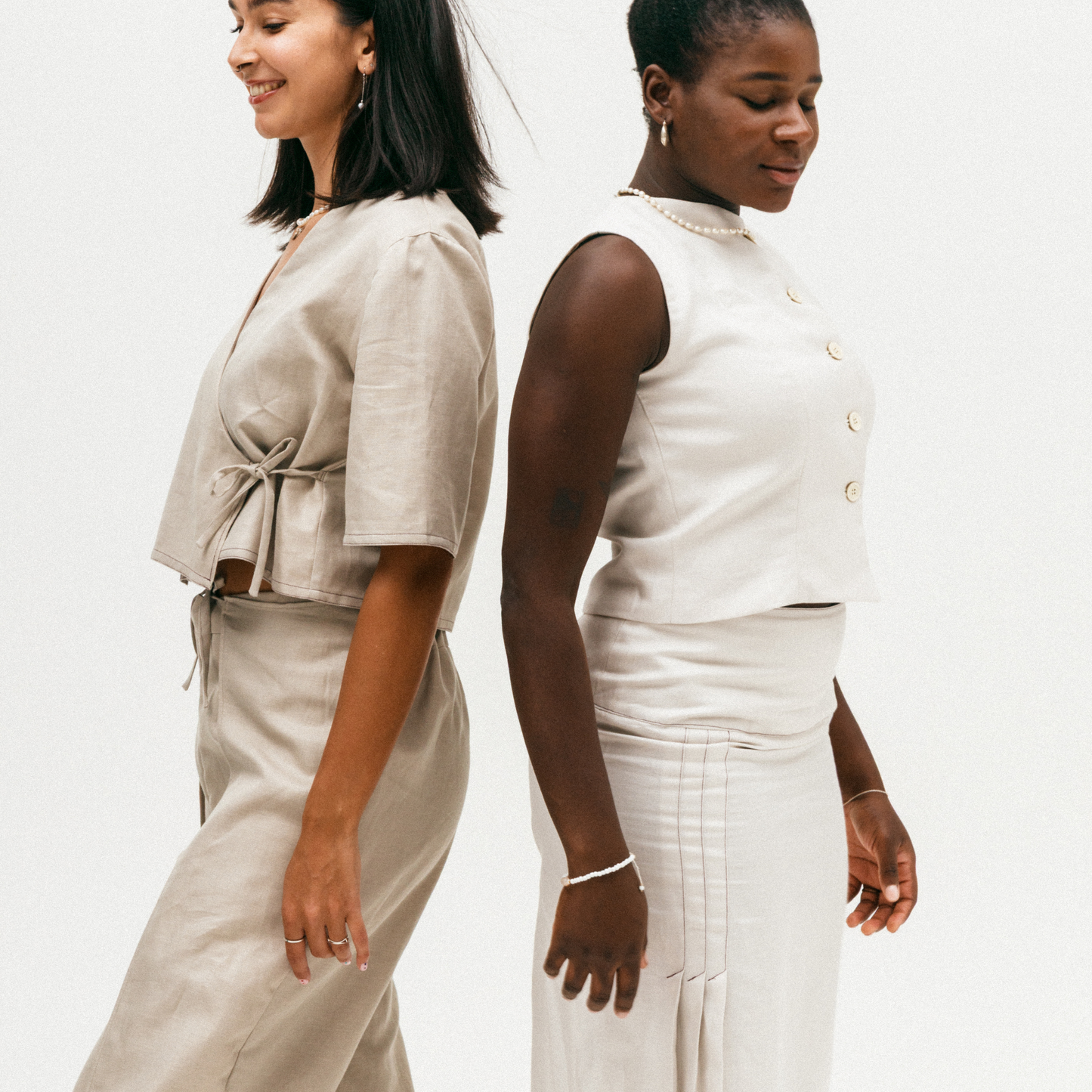 Two women wearing beige and white outfits against a plain background