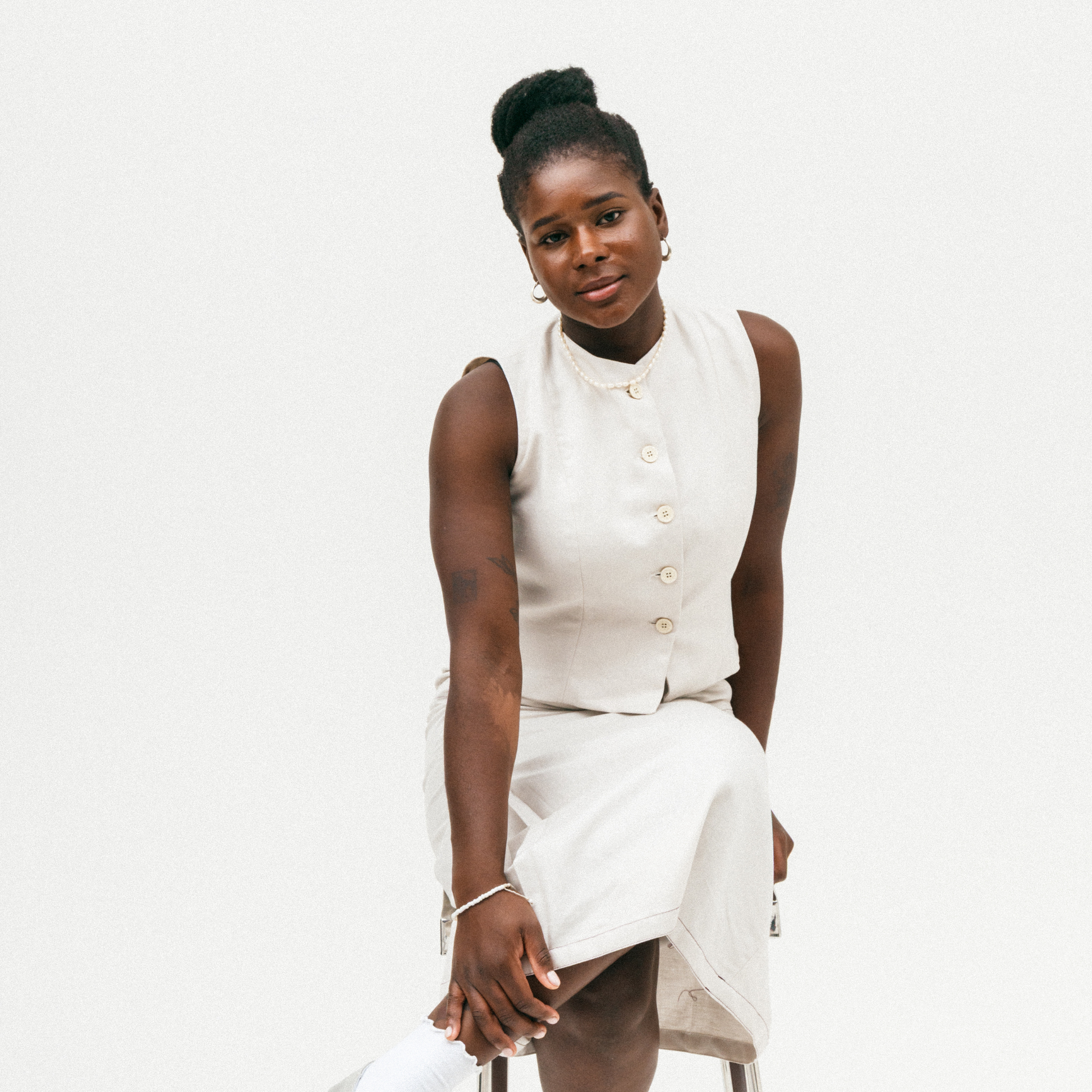 Woman wearing a white sleeveless top with white buttons and a white skirt on a white background