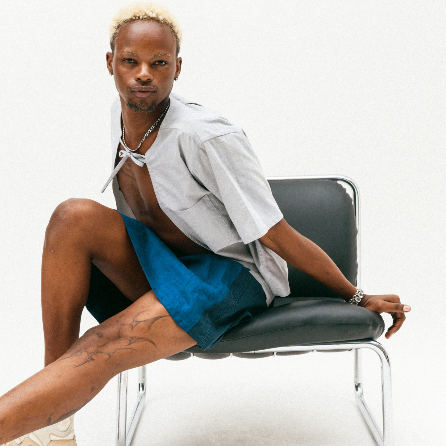 Person sat on a chair wearing a tailored grey, upcycled shirt with a structured silhouette and a bow.