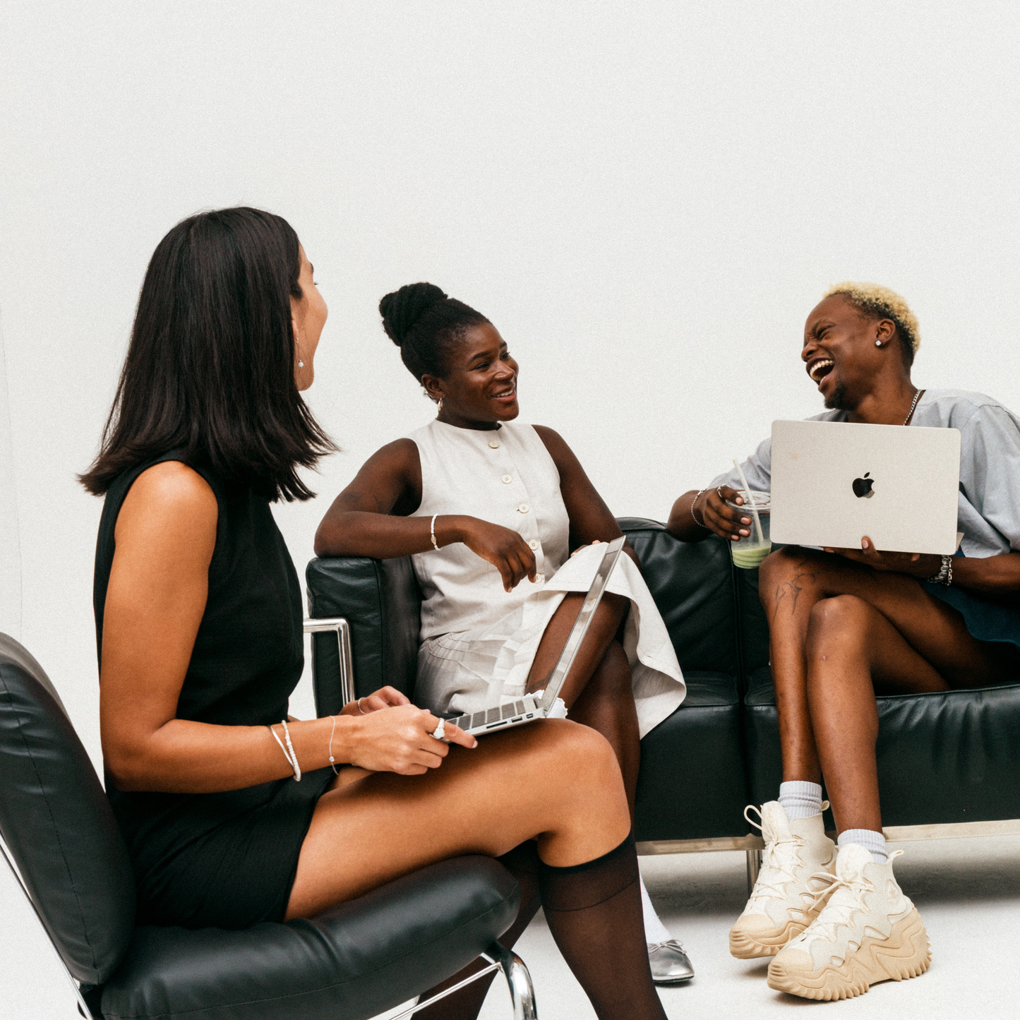 Three people sitting on a couch with laptops, engaged in conversation.