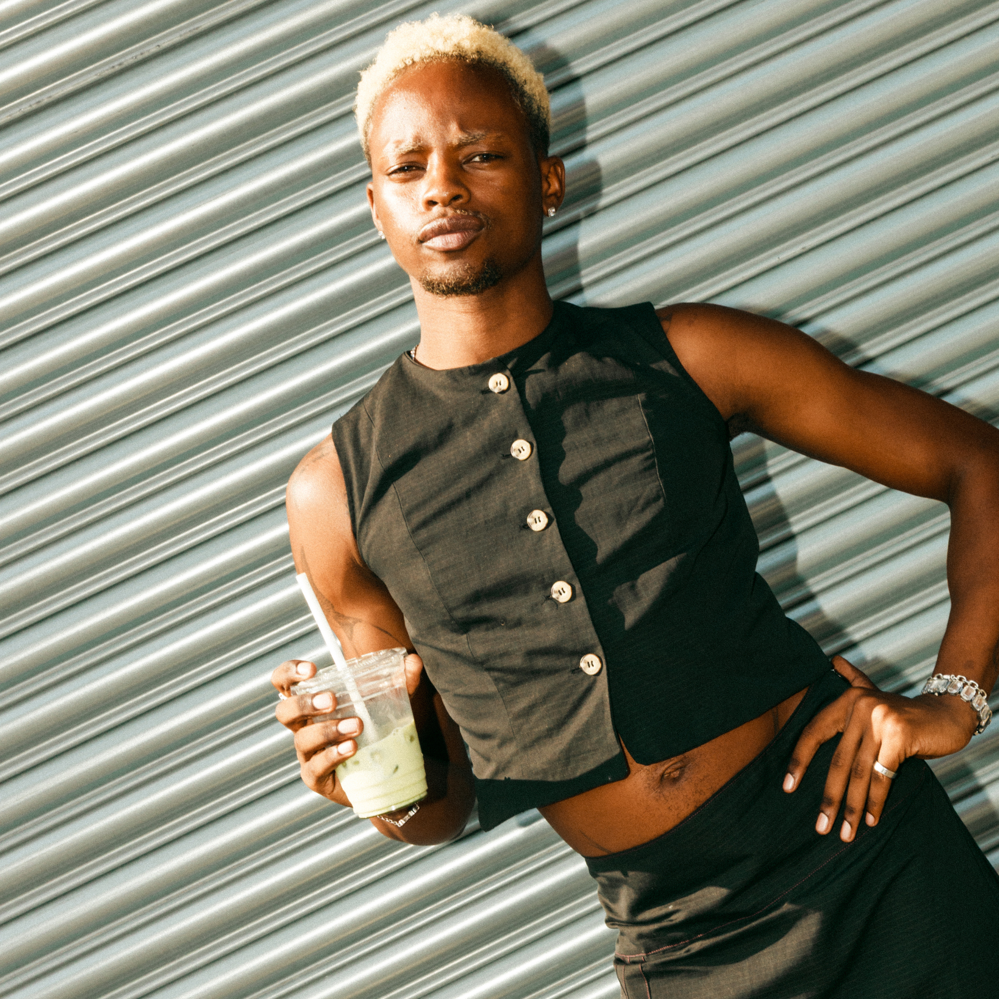 Person wearing a sleeveless button-up shirt against a corrugated metal background