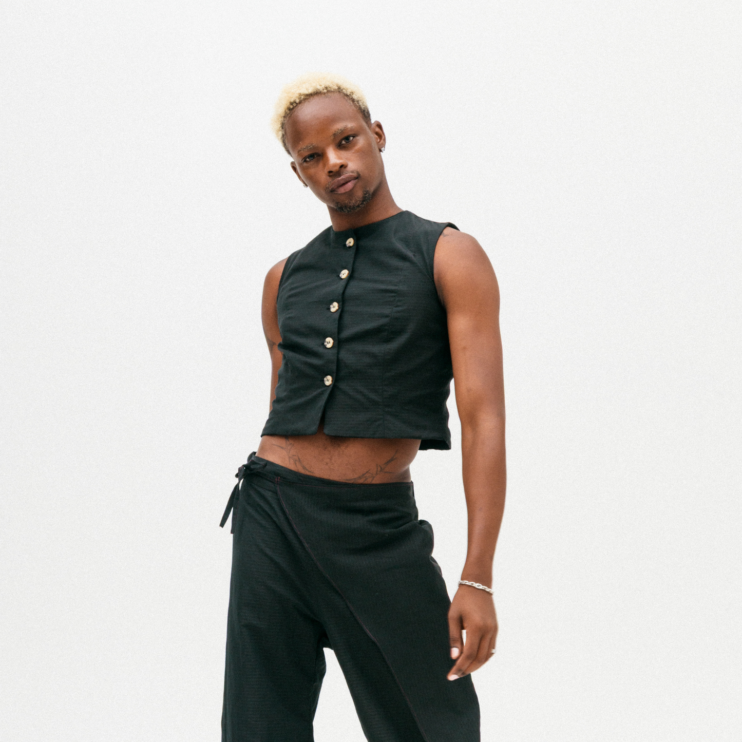Person wearing a black sleeveless top with buttons and black pants on a white background
