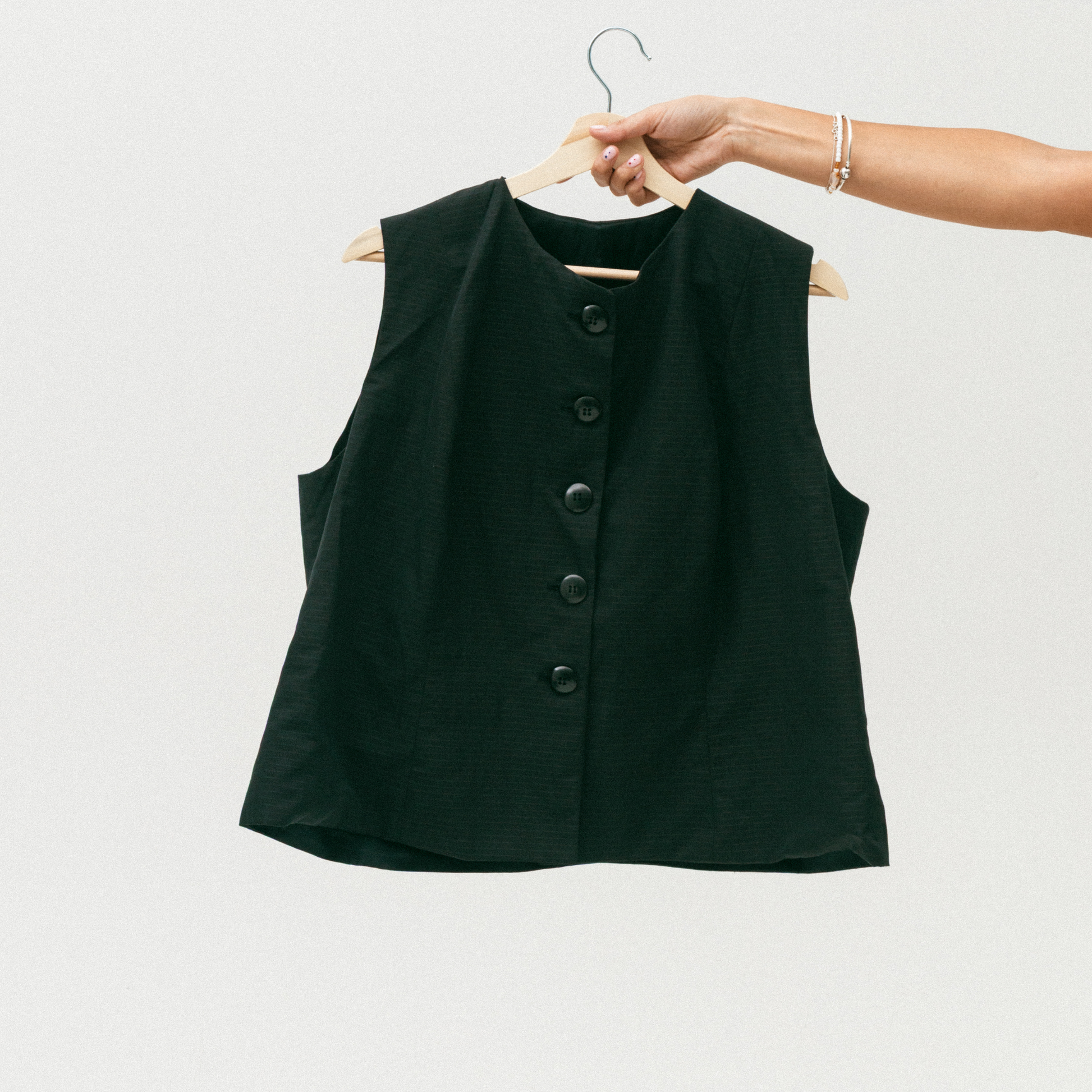 Black sleeveless button-up shirt on a hanger against a white background