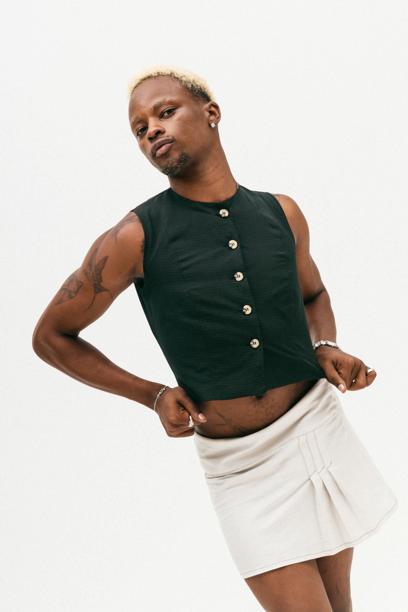 Person wearing a black sleeveless top with buttons and a white skirt on a light background