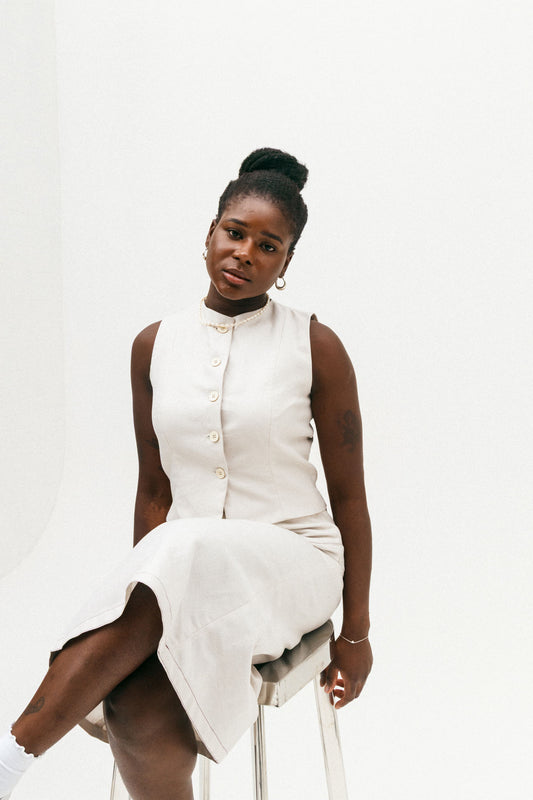 Woman wearing a white sleeveless dress sitting on a white stool against a white background