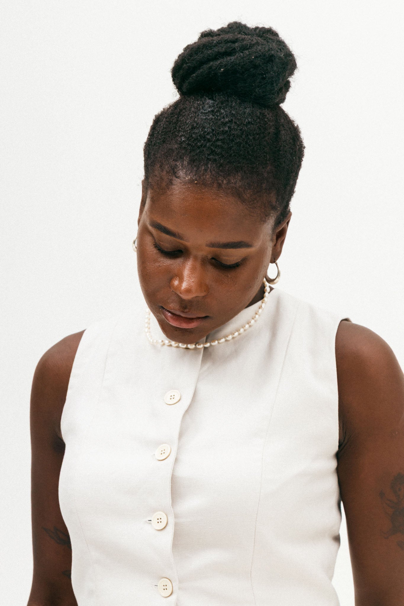 Woman wearing a white sleeveless top with buttons on a plain background
