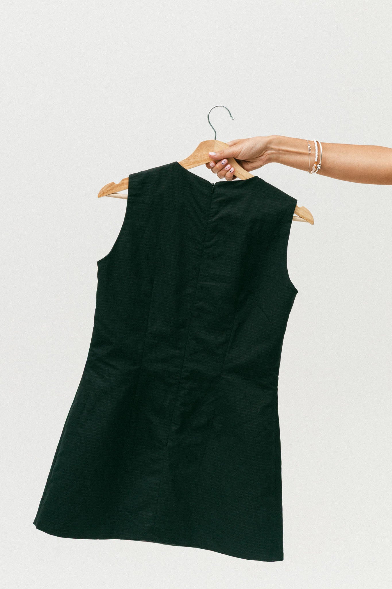 Black sleeveless dress on a hanger against a white background