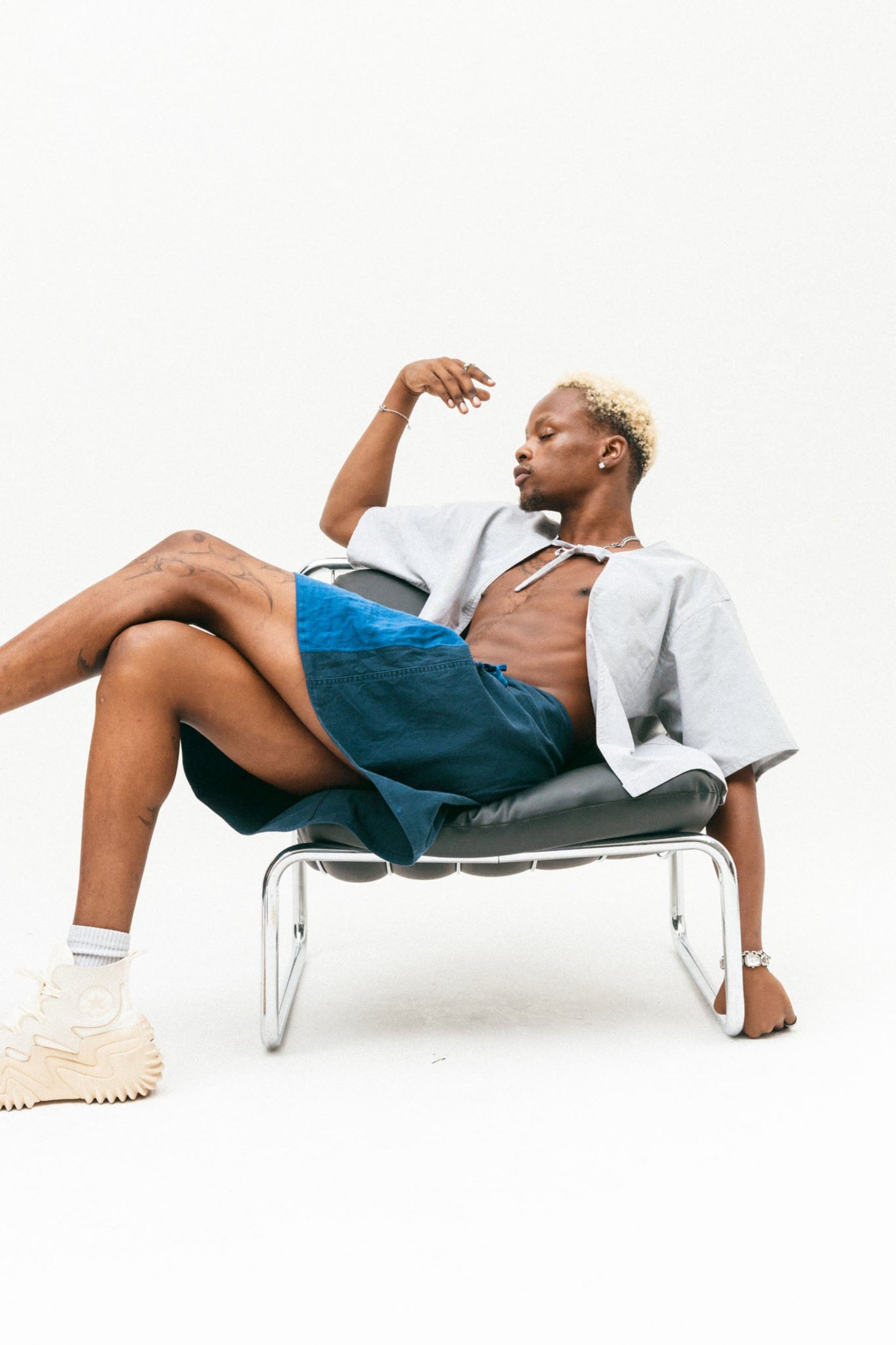 Person sat on a chair wearing a tailored grey, upcycled shirt with a structured silhouette and a bow and a tailored blue skirt.